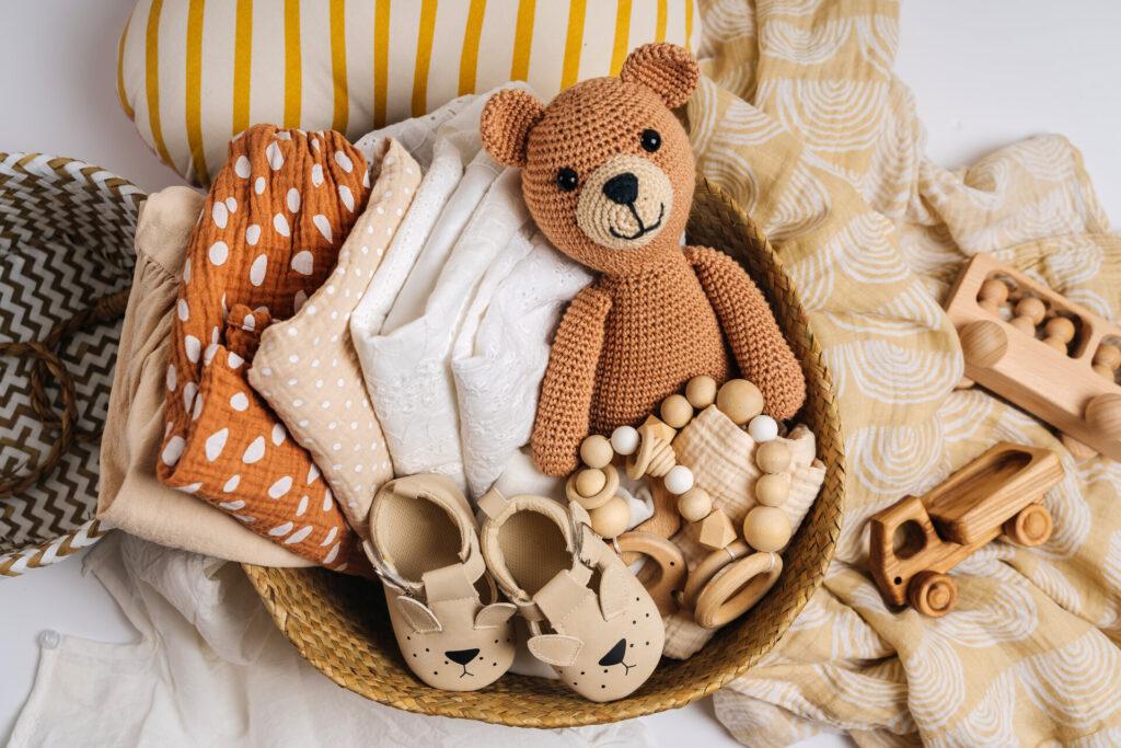 Korb mit Baby-Sachen und Zubehör für Neugeborene. Geschenkkorb mit Baumwolle Kleidung und Musselin swaddle Decke, Baby-Schuhe, Spielzeug und niedlichen Teddybär in beige Farben.