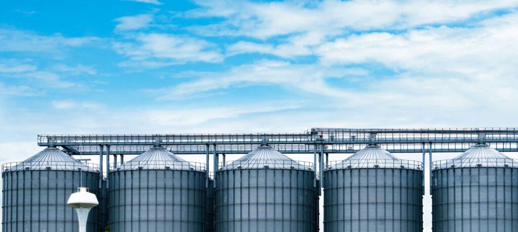 Mehrere große silberne Futtermitteltanks und Silos in einer Reihe, unter einem klaren blauen Himmel