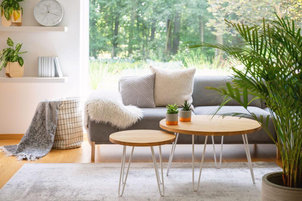 Modernes Wohnzimmer mit grauem Sofa, Pflanzen und einem minimalistischen Couchtisch aus Holz und Metall als stilvollem Mittelpunkt des Raumes.