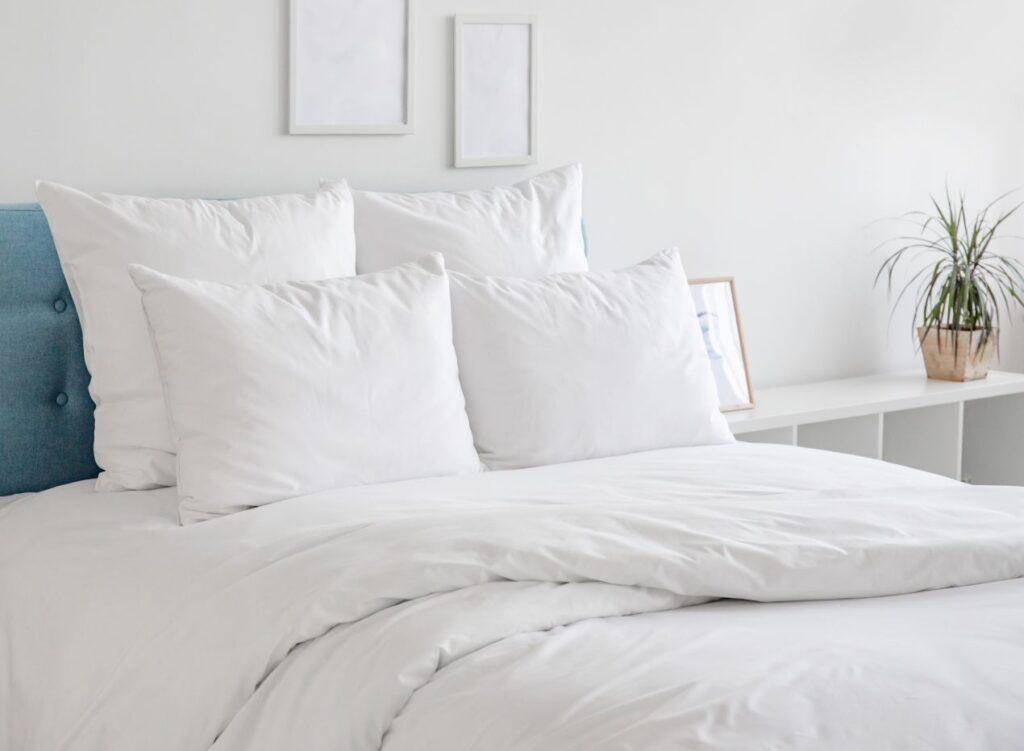 Modernes-Bett-mit-Matratzenschutz-und-weisser-Bettwaesche-in-heller-Schlafzimmerumgebung