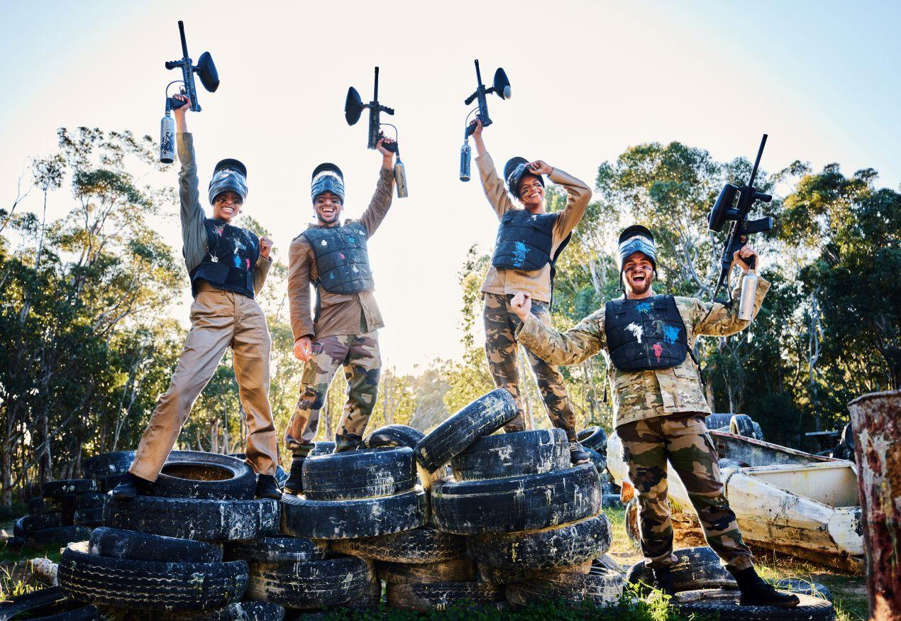 Vier Spieler jubeln nach Match bei Paintball Berlin auf einem Outdoor-Feld mit Tarnkleidung