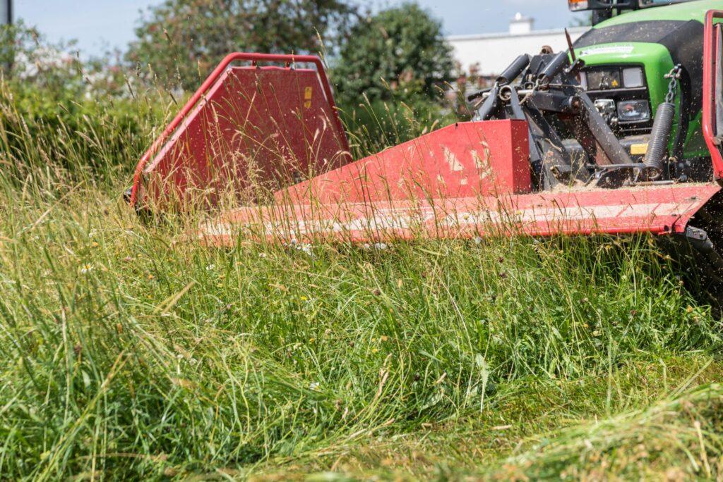 Detailaufnahme eines laufenden Schlegelmulchers am Traktor beim Zerkleinern von dichtem Wiesenbewuchs